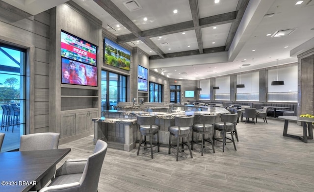 bar featuring beamed ceiling, light wood-type flooring, light stone countertops, and coffered ceiling