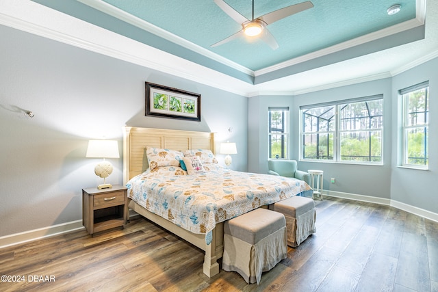 bedroom featuring dark hardwood / wood-style flooring, a tray ceiling, multiple windows, and crown molding