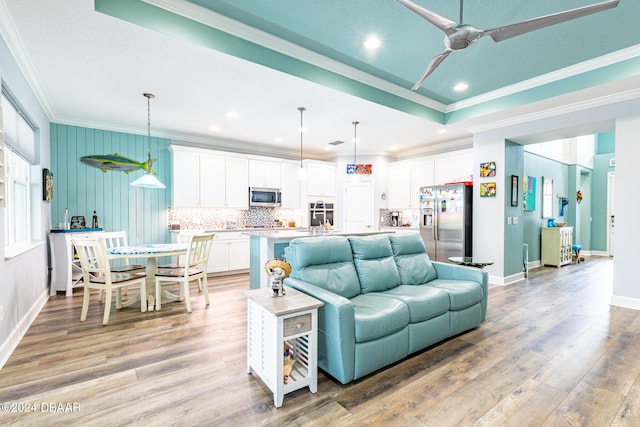 living room with ceiling fan, ornamental molding, a raised ceiling, and light hardwood / wood-style flooring