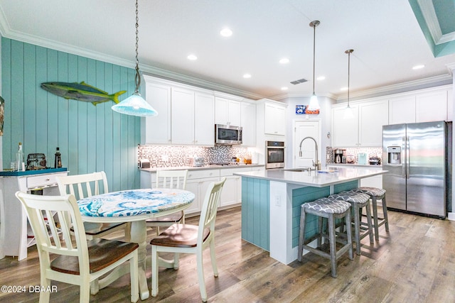 kitchen featuring stainless steel appliances, white cabinetry, an island with sink, and decorative light fixtures