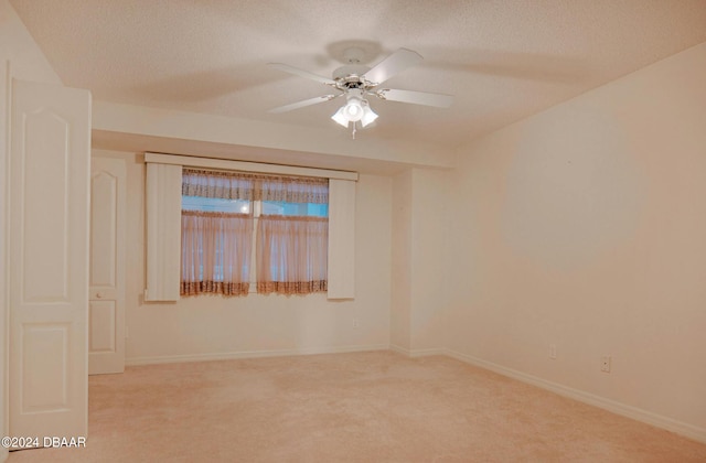 spare room with a textured ceiling, light colored carpet, and ceiling fan