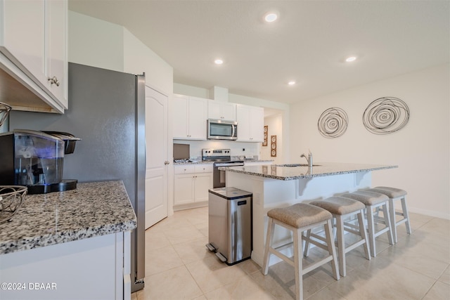 kitchen with light stone counters, a center island with sink, appliances with stainless steel finishes, light tile patterned floors, and white cabinets