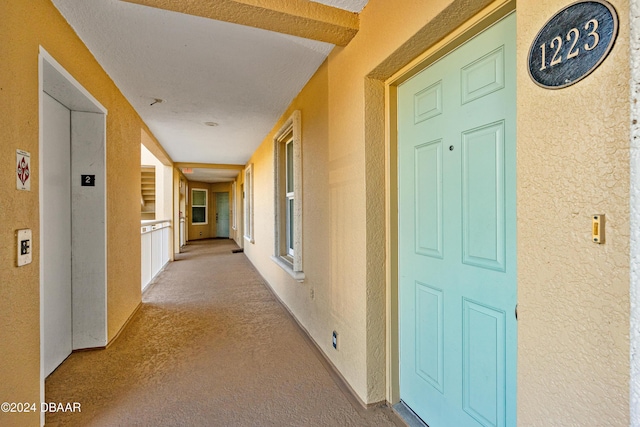 hallway featuring elevator, light colored carpet, and a textured ceiling