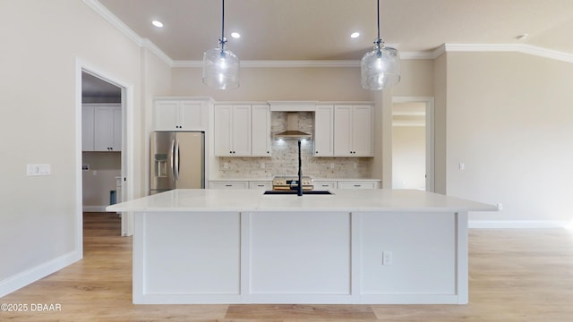 kitchen featuring wall chimney range hood, stainless steel fridge, a large island, and decorative light fixtures