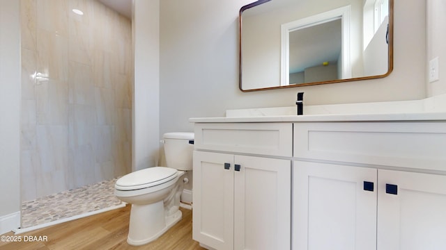 bathroom with toilet, wood finished floors, vanity, baseboards, and a tile shower