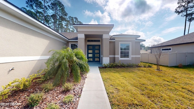 entrance to property featuring an attached garage, fence, a lawn, and stucco siding