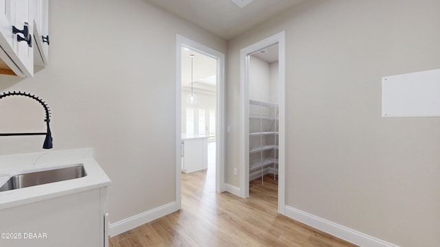 hall with light wood-style flooring, baseboards, and a sink