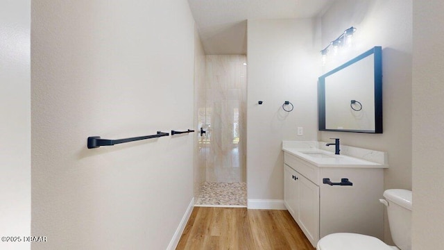 bathroom featuring baseboards, toilet, wood finished floors, vanity, and a walk in shower