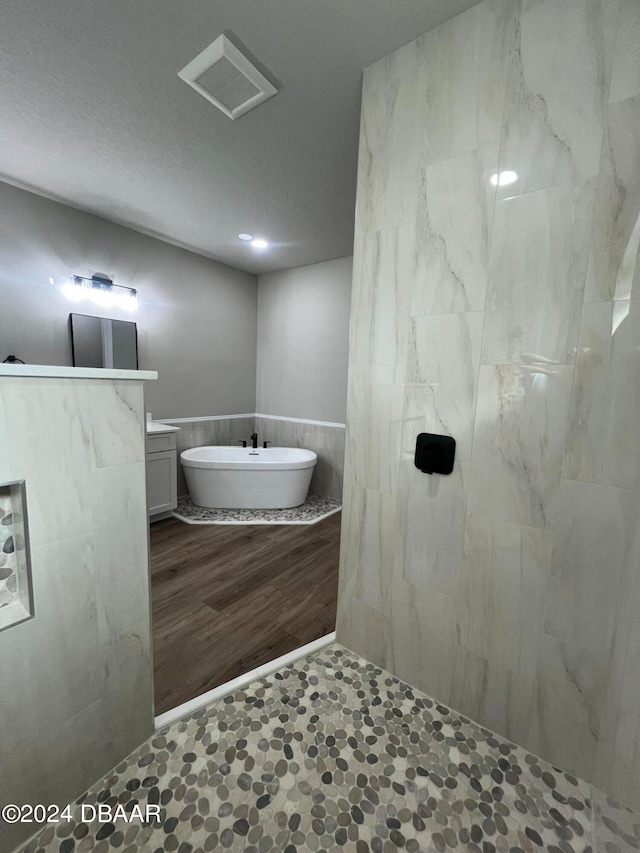 bathroom with a wainscoted wall, a textured ceiling, vanity, a freestanding tub, and a walk in shower