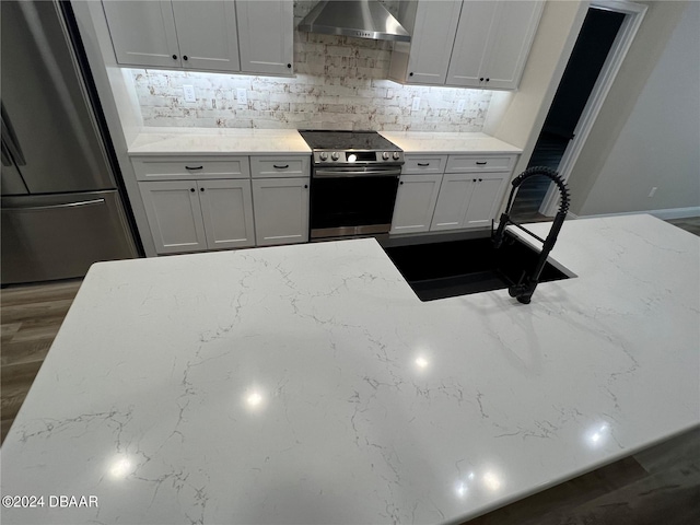 kitchen featuring stainless steel appliances, sink, light stone counters, white cabinets, and wall chimney range hood