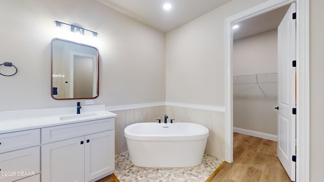 bathroom with a walk in closet, a wainscoted wall, a freestanding bath, vanity, and wood finished floors