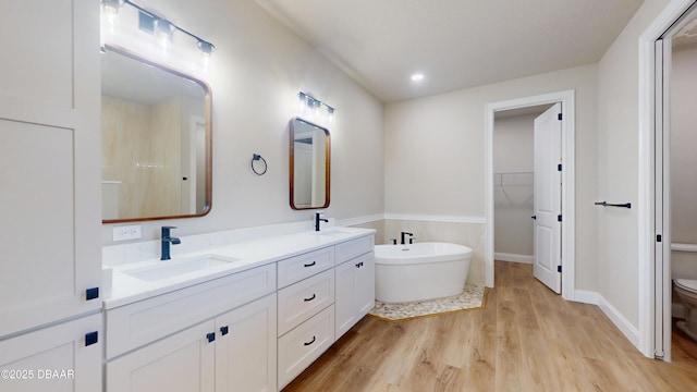 full bath featuring toilet, a soaking tub, wood finished floors, a walk in closet, and a sink