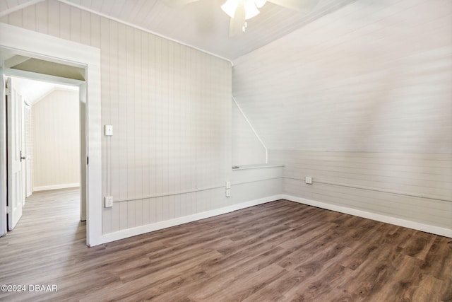 spare room featuring wood walls, ceiling fan, dark wood-type flooring, and vaulted ceiling