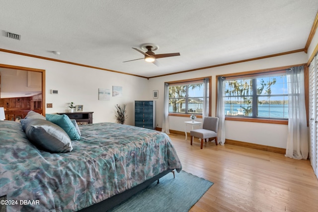 bedroom featuring a textured ceiling, light hardwood / wood-style floors, ceiling fan, and a water view