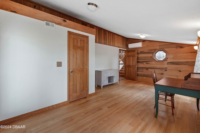 dining area with a wall unit AC, wood walls, light hardwood / wood-style floors, and vaulted ceiling