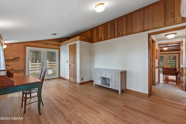 interior space with french doors, wood walls, a textured ceiling, vaulted ceiling, and light wood-type flooring