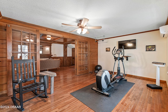 exercise room featuring ceiling fan, a wall mounted air conditioner, a textured ceiling, wooden walls, and hardwood / wood-style flooring