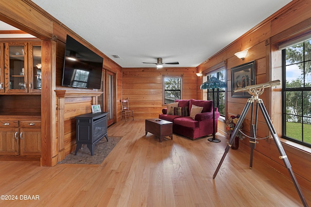 living room featuring a wood stove, wooden walls, light hardwood / wood-style flooring, and a healthy amount of sunlight