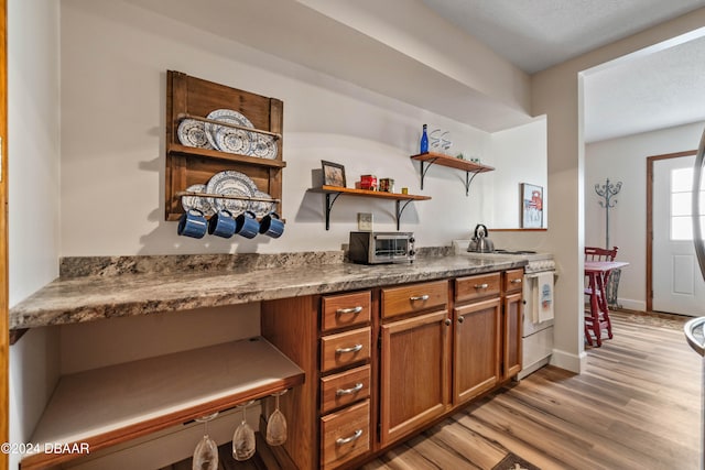 kitchen with light wood-type flooring, a textured ceiling, stainless steel range, and dark stone counters