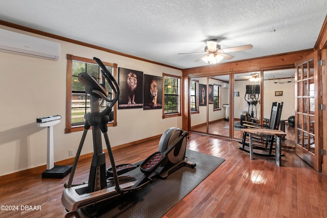 exercise room with a wall mounted air conditioner, crown molding, hardwood / wood-style flooring, ceiling fan, and a textured ceiling