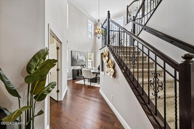 stairway featuring hardwood / wood-style flooring, a towering ceiling, crown molding, and a notable chandelier