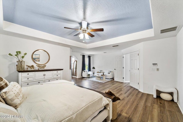 bedroom with hardwood / wood-style flooring, ceiling fan, a textured ceiling, and a tray ceiling