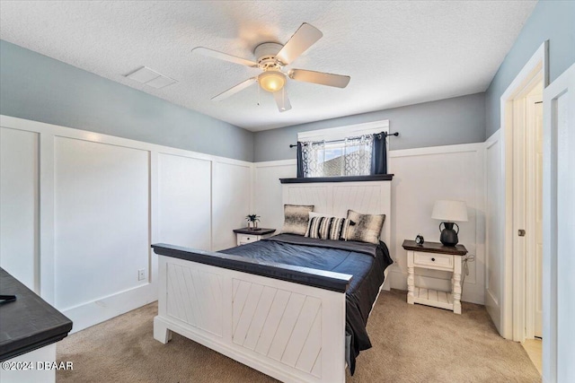 bedroom with a textured ceiling, multiple closets, light carpet, and ceiling fan