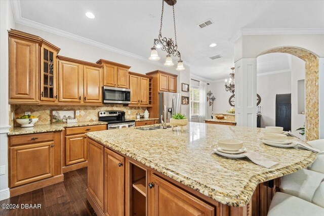 kitchen with light stone counters, appliances with stainless steel finishes, ornamental molding, dark hardwood / wood-style floors, and an inviting chandelier