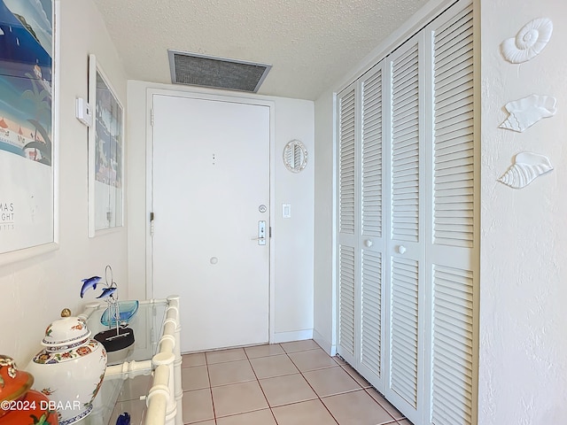 doorway with a textured ceiling and light tile patterned floors