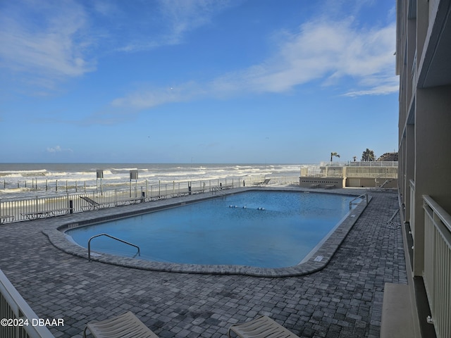 community pool with fence, a patio, a beach view, and a water view
