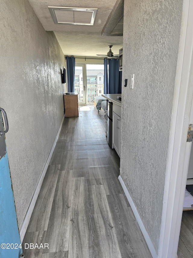 hallway featuring dark wood-type flooring, a textured wall, visible vents, and baseboards