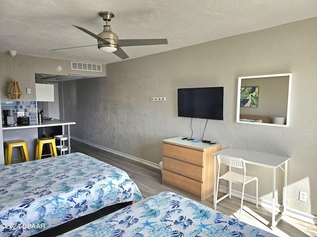 bedroom featuring wood finished floors, visible vents, a ceiling fan, a textured wall, and baseboards