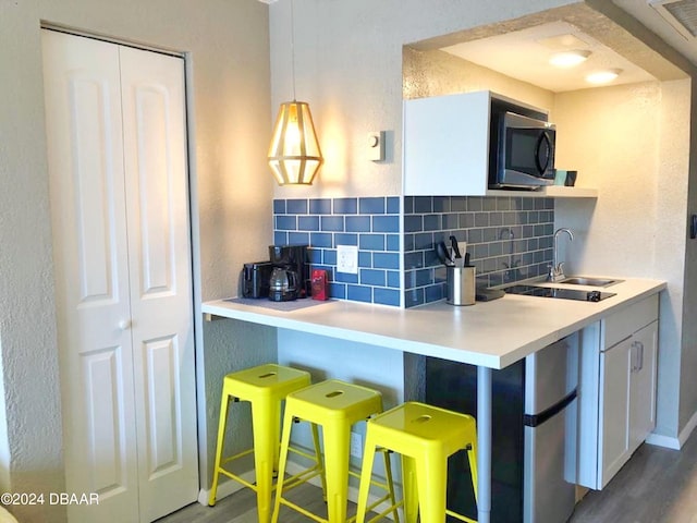 kitchen with white cabinets, a kitchen breakfast bar, wood finished floors, a sink, and decorative backsplash