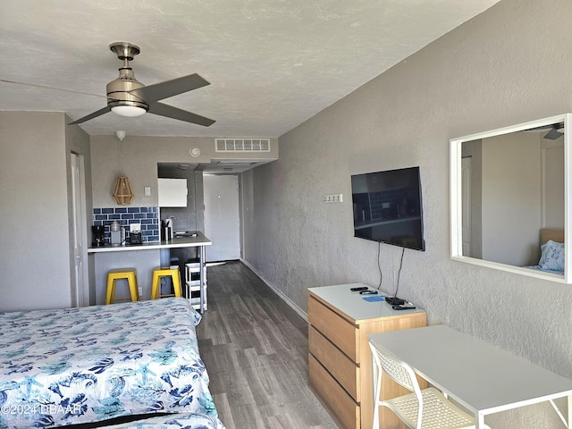 bedroom with a textured wall, baseboards, visible vents, and dark wood finished floors