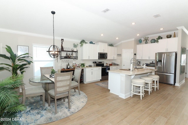 kitchen with appliances with stainless steel finishes, hanging light fixtures, white cabinets, lofted ceiling, and a kitchen island with sink