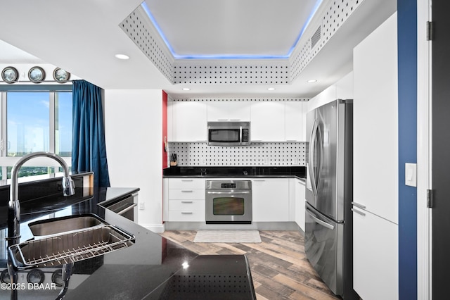 kitchen with white cabinets, a sink, dark countertops, stainless steel appliances, and backsplash
