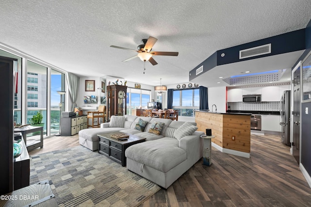 living area with a healthy amount of sunlight, dark wood-type flooring, visible vents, and ceiling fan