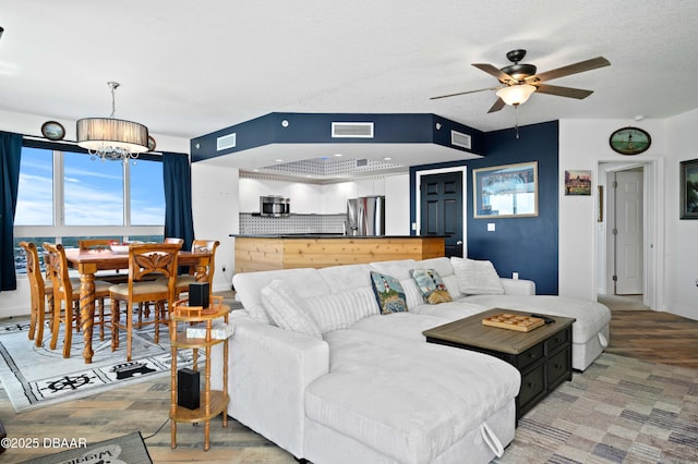 living room with a textured ceiling, ceiling fan with notable chandelier, and visible vents