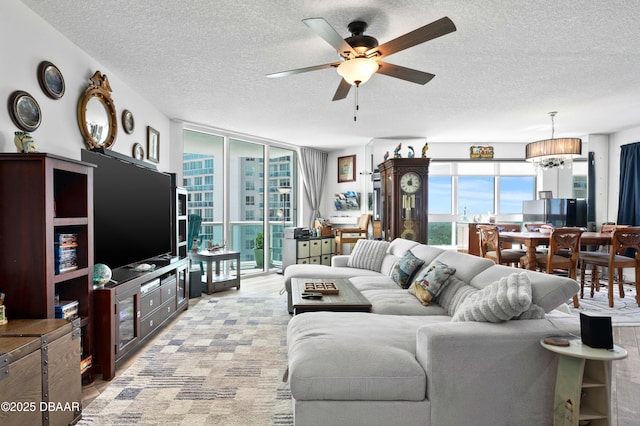 living room featuring expansive windows, ceiling fan with notable chandelier, a textured ceiling, and a healthy amount of sunlight