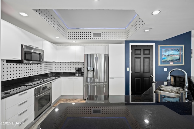 kitchen featuring tasteful backsplash, white cabinetry, dark countertops, stainless steel appliances, and a sink