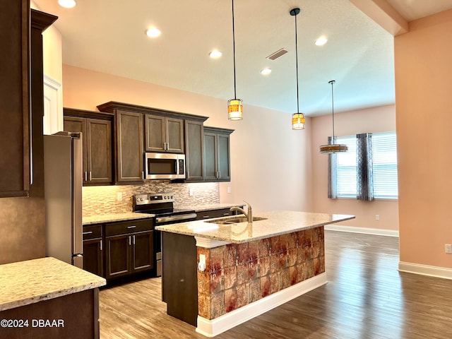 kitchen with pendant lighting, appliances with stainless steel finishes, light stone counters, and a kitchen island with sink