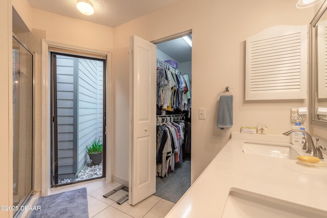 bathroom with tile patterned floors, a walk in closet, a textured ceiling, a shower stall, and a sink