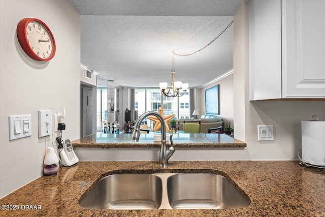 4505 S Atlantic Ave Unit 605, Ponce Inlet, FL 32127 - kitchen with dark stone counters, a textured ceiling, a chandelier, white cabinetry, and crown molding