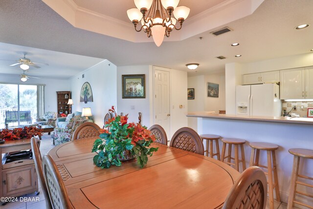 dining area with ceiling fan with notable chandelier, a raised ceiling, light tile patterned floors, and crown molding