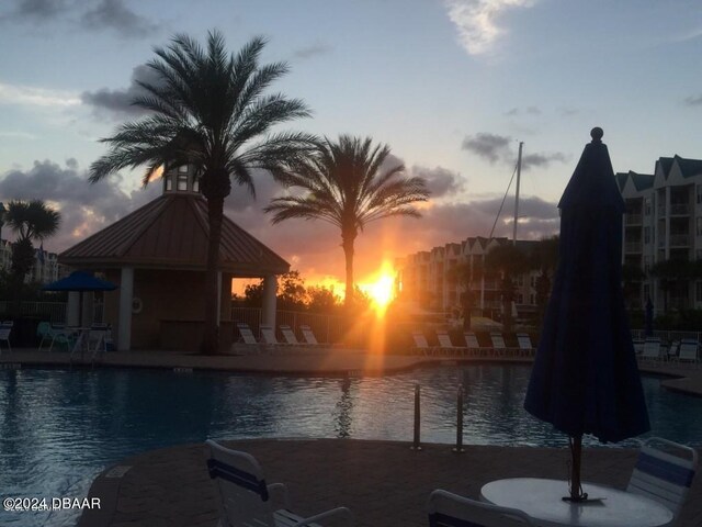 pool at dusk with a gazebo, a patio, and a water view