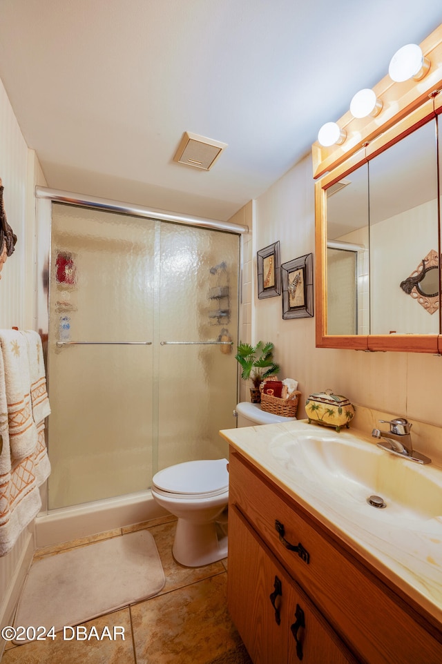 bathroom with toilet, vanity, tile patterned floors, and a shower with shower door