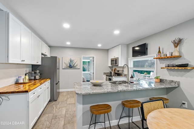 kitchen featuring appliances with stainless steel finishes, light stone countertops, a kitchen breakfast bar, white cabinets, and kitchen peninsula