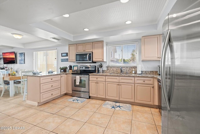 kitchen featuring stainless steel appliances, a raised ceiling, light tile patterned flooring, kitchen peninsula, and light stone countertops