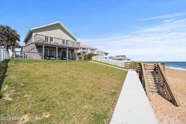 back of property with a yard, a deck with water view, and a view of the beach