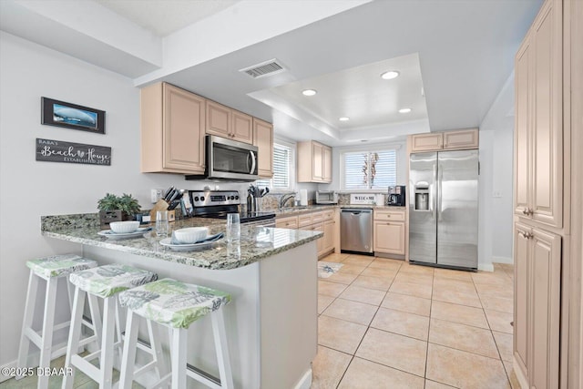 kitchen featuring light stone countertops, kitchen peninsula, a tray ceiling, appliances with stainless steel finishes, and light tile patterned flooring